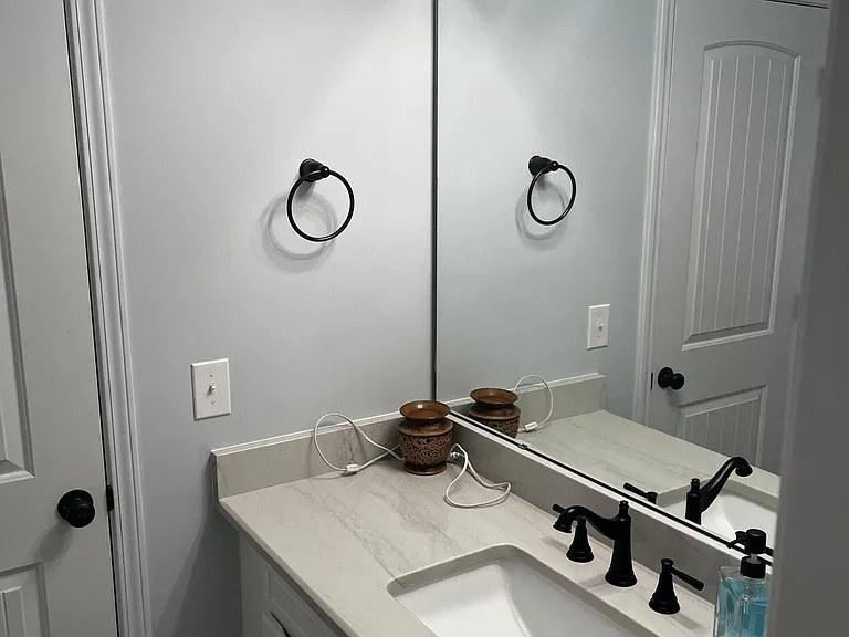 Jack and Jill bathroom vanity with ample storage, large mirror, house matching quartzite counter, and modern black fixtures.