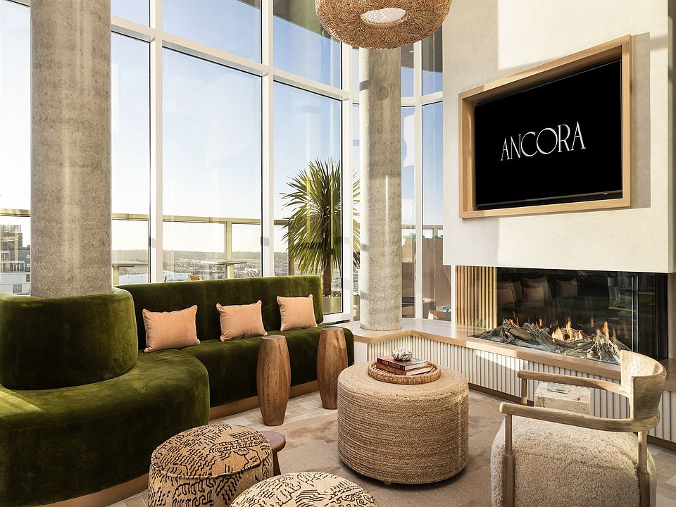 Luxurious apartment living room featuring a modern green velvet sofa, large windows with stunning views, a cozy fireplace, and elegant decor.