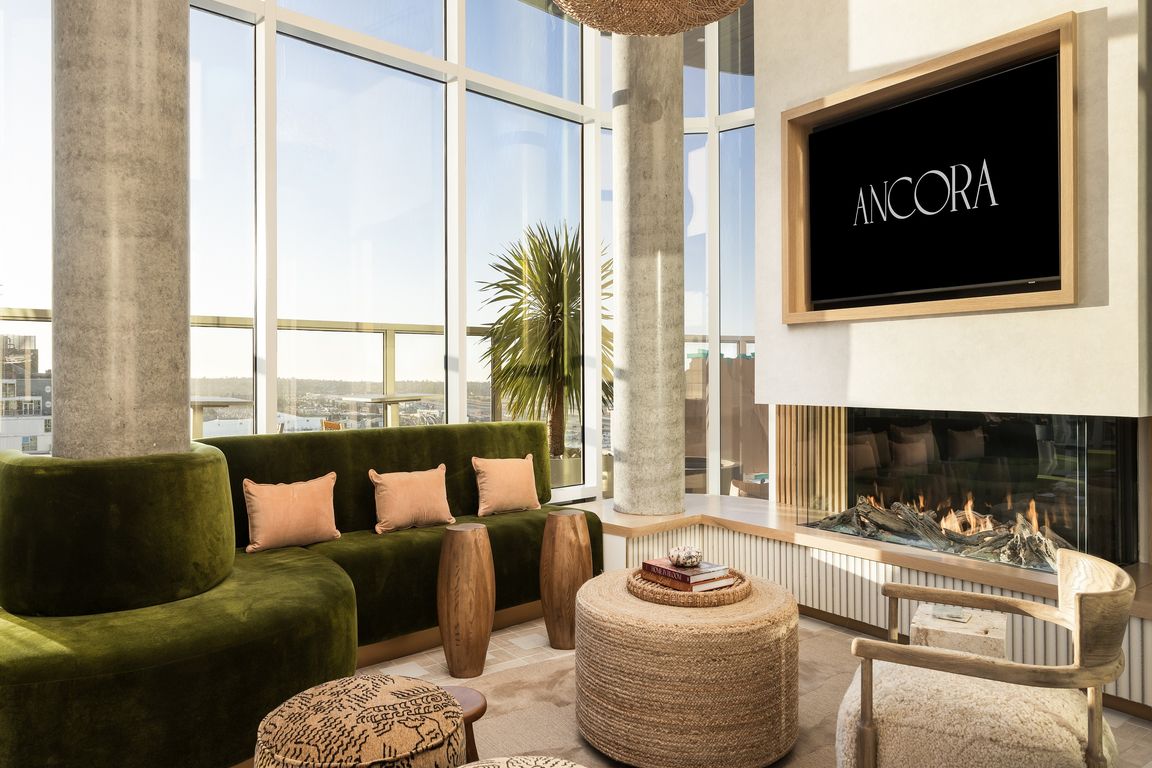 Luxurious apartment living room featuring a modern green velvet sofa, large windows with stunning views, a cozy fireplace, and elegant decor.