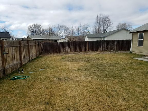 Large backyard with automatic sprinkler system and cement pad for outdoor living.