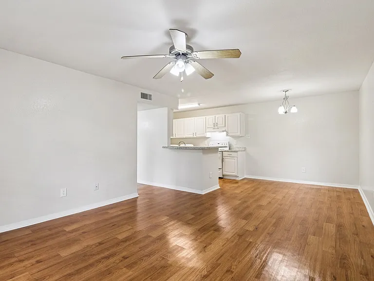 Bright open-concept space featuring elegant wood-style flooring, a modern kitchen with white cabinetry, and a ceiling fan for comfort. Bright open-concept space featuring elegant wood-style flooring, a modern kitchen with white cabinetry, and a ceiling fa