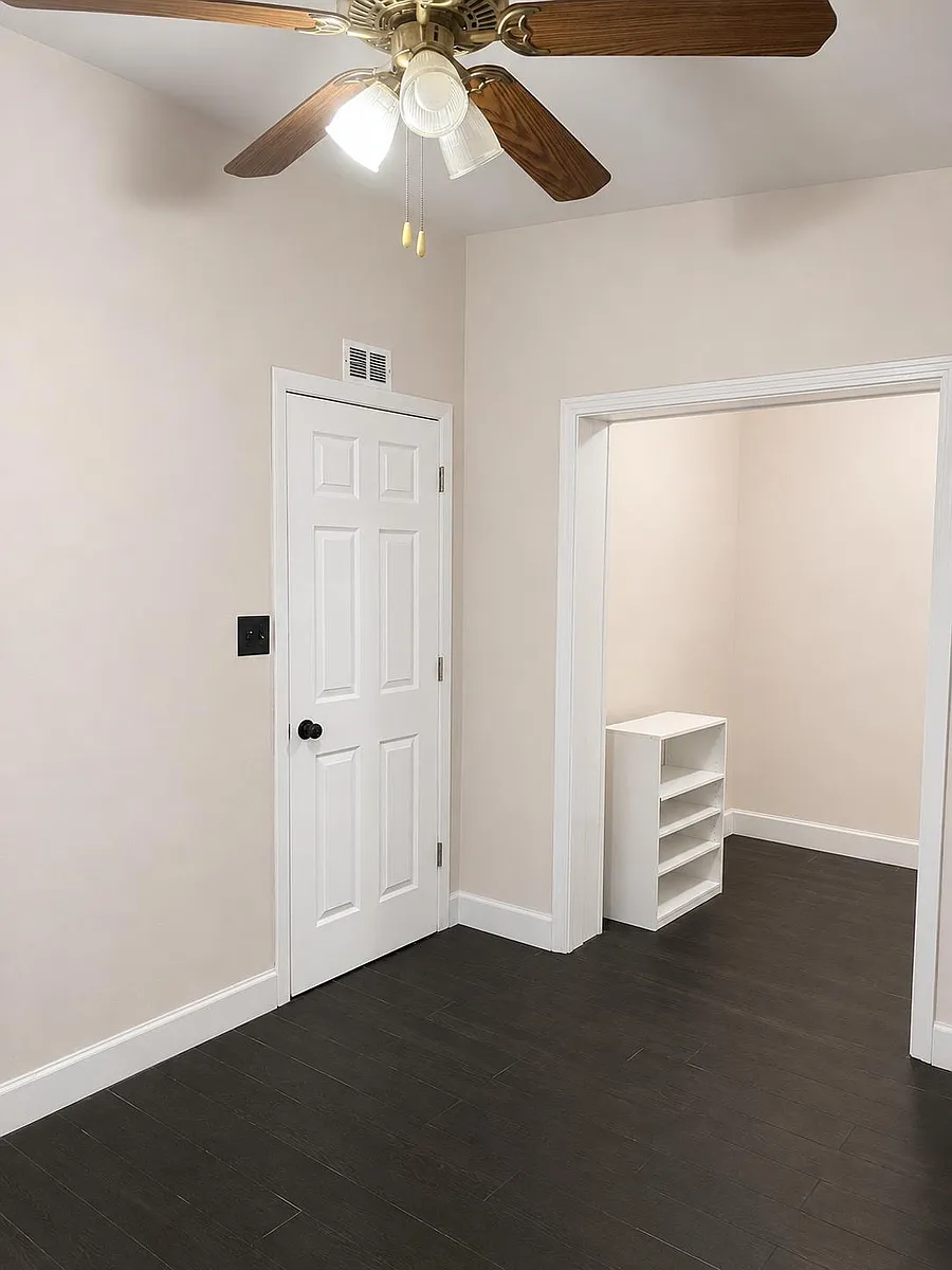 Freshly finished room with durable dark flooring, ceiling fan lighting, and a walk-in closet area with shelving. - Harold Bedford Rd