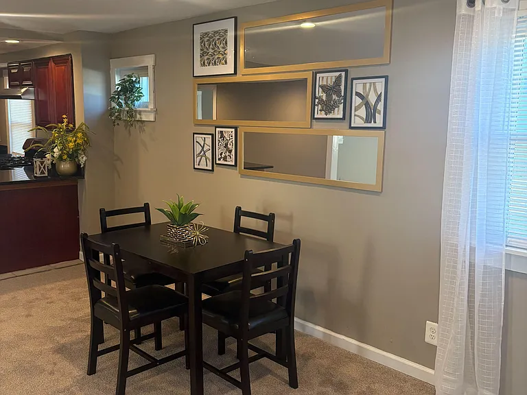 Dining area with a four-seat table, recessed lighting, and a window with sheer curtains, adjacent to the kitchen.