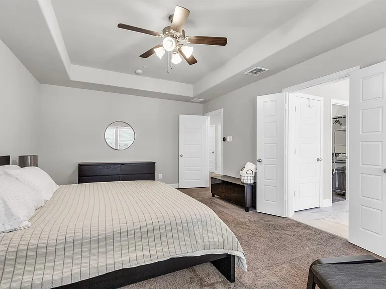 Spacious interior featuring a tray ceiling with a ceiling fan, light gray wall paint, and a circular wall mirror