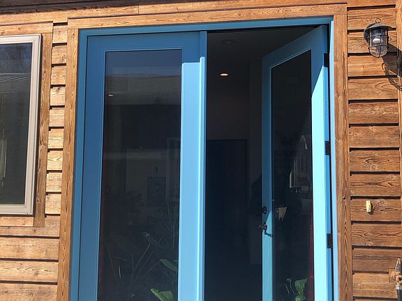 Powder-blue French doors serve as the main entry, framed by cedar siding and a wall-mounted exterior light fixture.