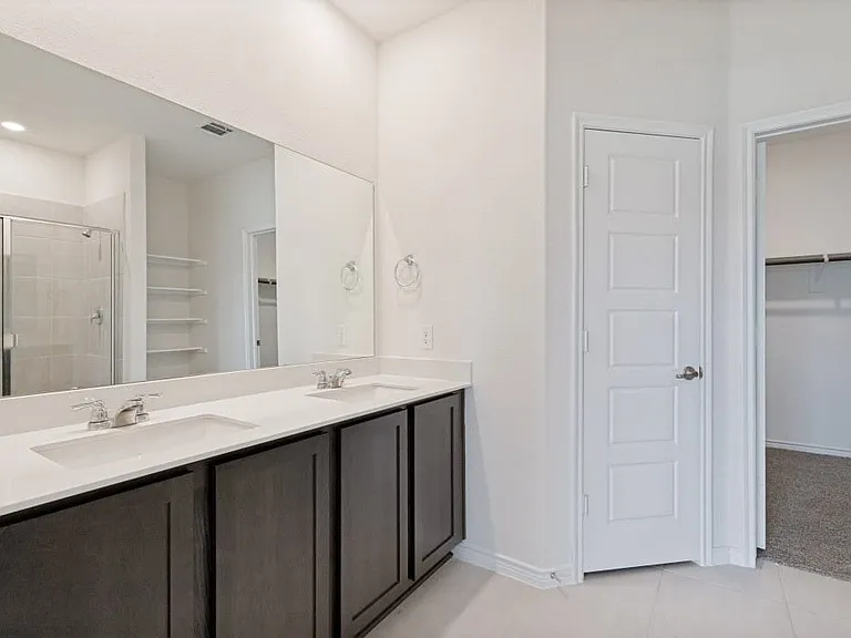 Bathroom featuring a dual vanity with undermount sinks, white countertops, dark wood cabinetry, a large wall-mounted mirror, and tile flooring
