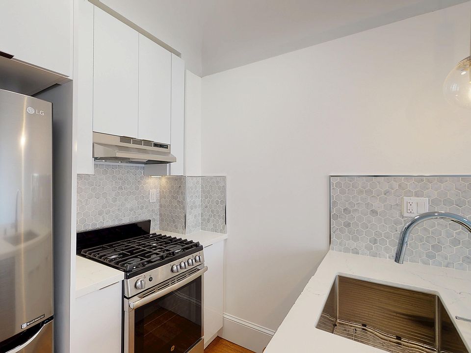 Kitchen with stainless fridge, gas stove, cabinets, hex tile backsplash, pendant light