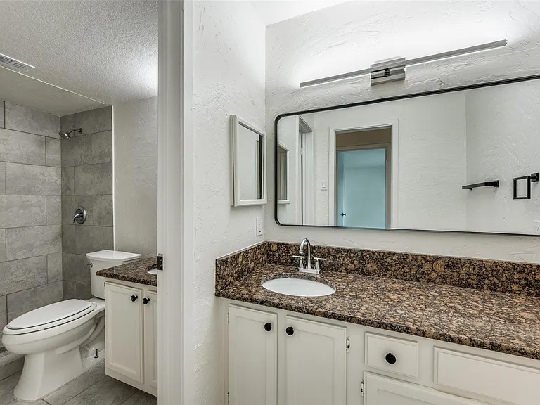 Bathroom featuring a single vanity with a granite-style countertop, undermount sink, and chrome faucet