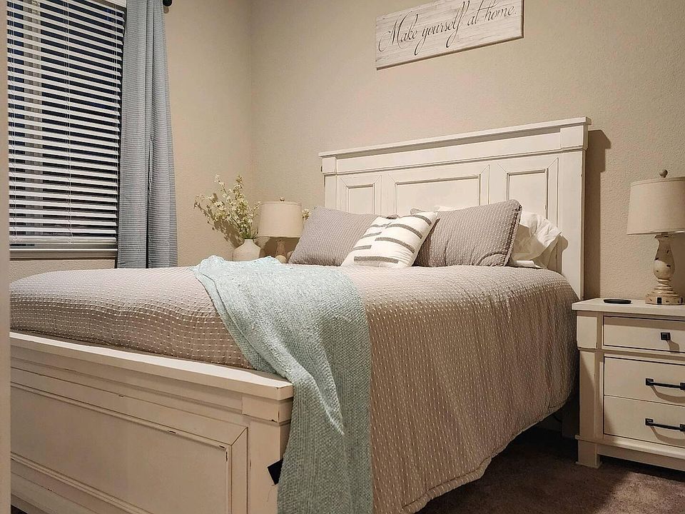 Bedroom with fan and tv with side night stands with lamps. Window blinds and drapes to darken room