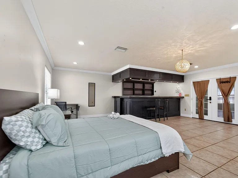 Spacious bedroom suite with a dedicated desk area, built-in bar with seating, and French doors for added access and light.