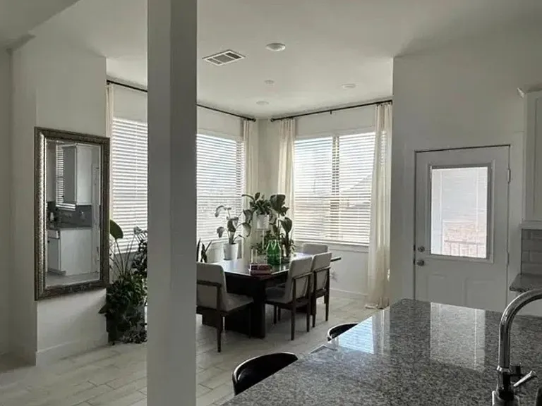 Open dining area with large corner windows, adjacent to a kitchen with granite counters and a door to the exterior.