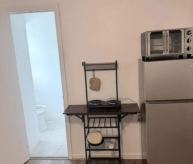 Compact kitchenette area featuring a full-size refrigerator, countertop microwave, and open shelving for storage.