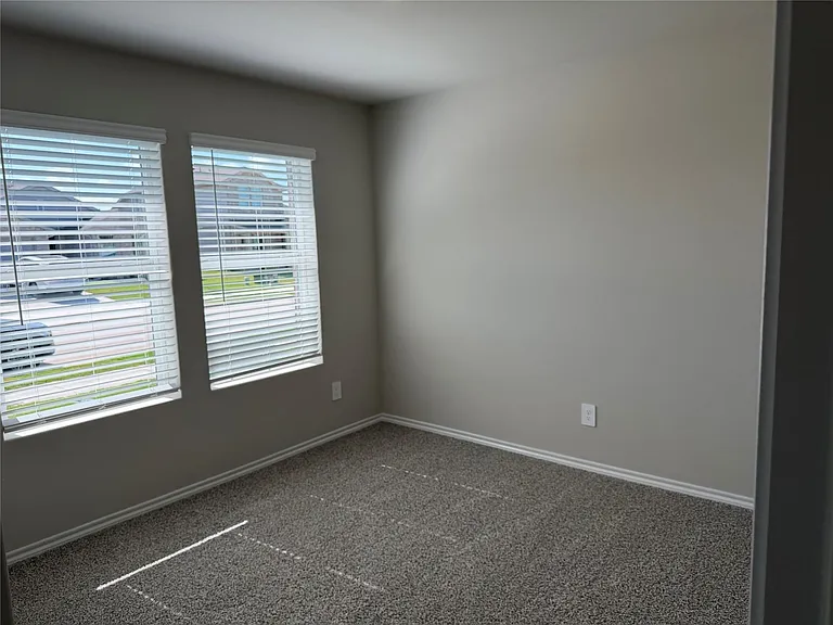 Neutral-toned interior room featuring two windows with white blinds, light gray walls, and dark gray textured carpeting