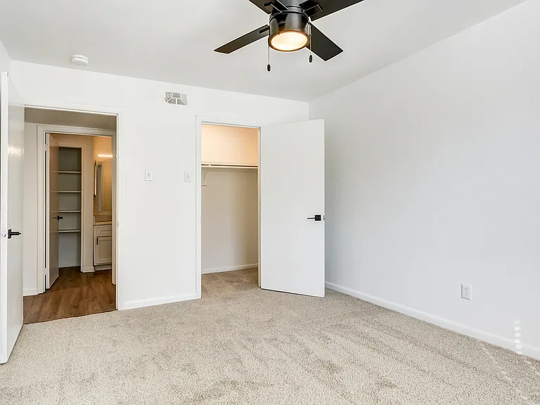 A carpeted bedroom with oversized closet and ceiling fan is shown at ReNew on Cantrell.