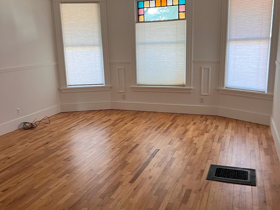 Spacious living room with gleaming hardwood floors, bay windows, and colorful stained glass accent. Bright and inviting space with tons of natural light.