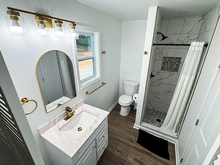 Updated full bath with a quartz-top vanity, gold-tone fixtures, and a tiled walk-in shower with built-in niche.