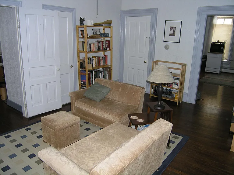 Living room. Open door on left leads to the bedroom. Closed door partially covered by the open bedroom door is a closet. Other closed door leads to the basement. Open archway on the right leads to the kitchen.