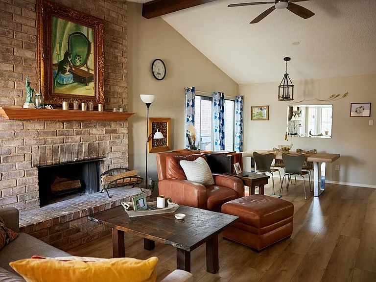 Living area with a ceiling fan, wood finished floors, beam ceiling, a brick fireplace, and high vaulted ceiling