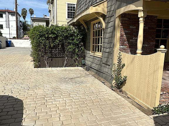 One car assigned parking spot against yellow fence and living room window between patio fence and locking shed, not shown.