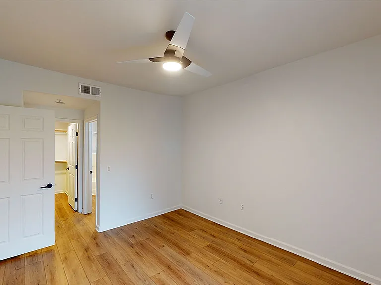 Spacious apartment bedroom with large closet, attached bathroom and wood style flooring.