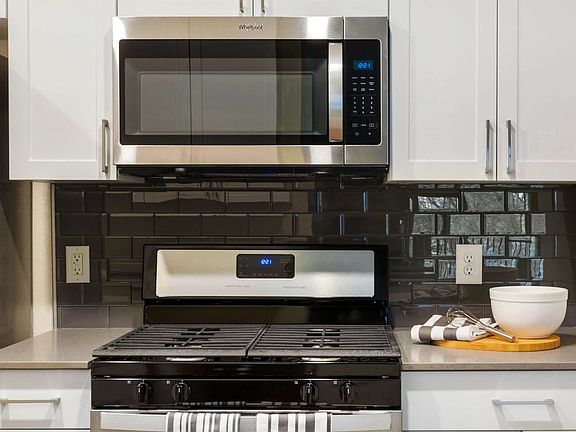Renovated Package I kitchen with white cabinetry, grey quartz countertops, glass tile backsplash, and stainless steel appliances, and hard surface plank flooring
