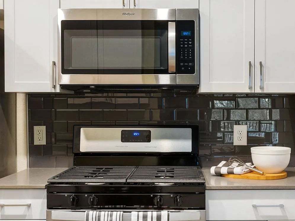 Renovated Package I kitchen with white cabinetry, grey quartz countertops, glass tile backsplash, and stainless steel appliances, and hard surface plank flooring - Avalon at Lexington