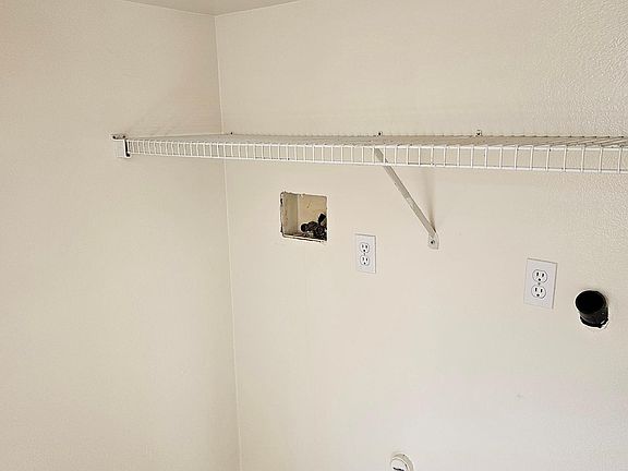View of the laundry area with hookups for washer and gas dryer. Note the shelf for laundry supplies.