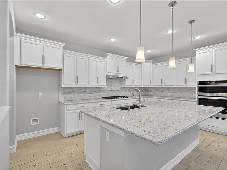 Modern kitchen featuring white cabinetry, light-toned countertops, a central island with an undermount sink, built-in double ovens, and recessed lighting