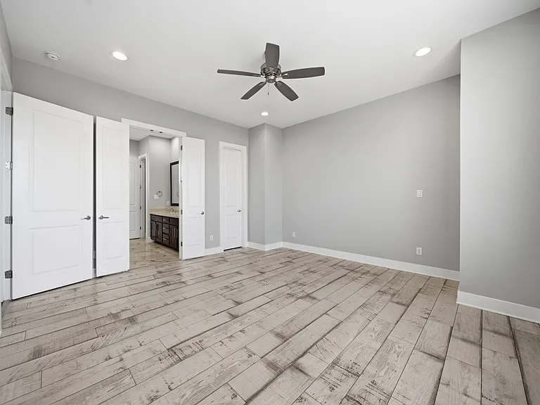 Spacious and light-filled primary bedroom featuring modern wood flooring and elevated finishes throughout. Large windows bring in abundant natural light, complemented by recessed lighting and a ceiling fan. Double doors lead to a private en-suite bath.
