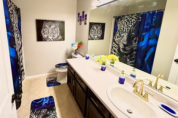 The bathroom features a sleek, modern aesthetic with clean lines and a neutral color palette. A striking black and white tiger painting adds drama and personality to the space. With ample coun