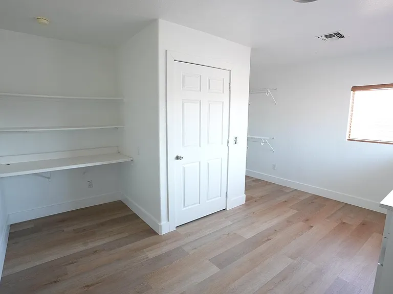 Spacious room with wood-look flooring, window with blinds, and built-in desk and shelving for work or study.