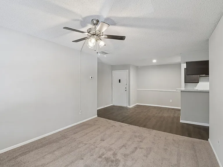 Inviting living space featuring plush carpet, sleek hardwood floor transition, and modern ceiling fan in an open layout apartment.