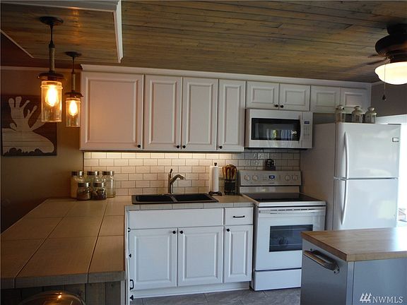 Kitchen with large bay window to riverfront deck has new cabinets, lighting, appliances, & flooring with custom wood accents