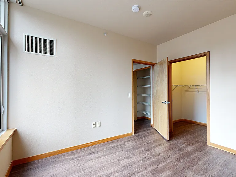 Spacious apartment bedroom with large closet and wood-style flooring.