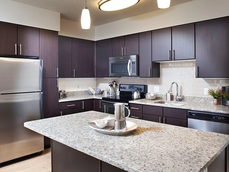 Classic Package kitchen with grey granite countertops, espresso cabinetry, stainless steel or black appliances, tile backsplash, and hard surface flooring (in select homes)