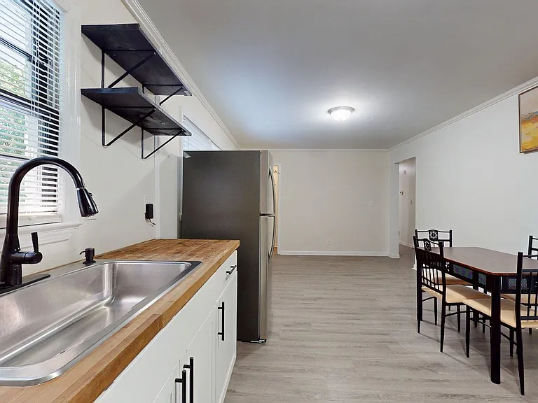 Open kitchen and dining area with butcher-block counters, stainless sink, and full-size fridge, plus space for a table.