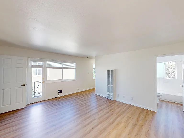 Bright and inviting living room with sleek hardwood floors, large window providing natural light, and an accessible door leading to the outdoors. Bright and inviting living room with sleek hardwood floors, large window providing natural light, and an acce