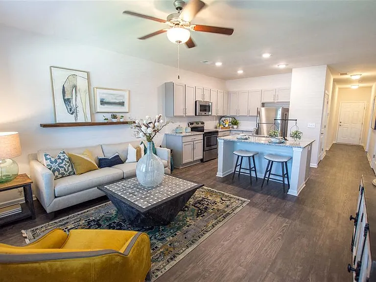 Living room with large windows that let in a ton of natural light looking into the kitchen.