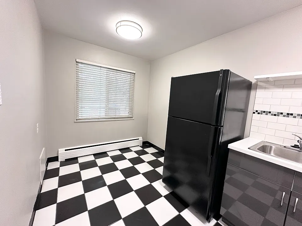 Charming kitchen with contemporary black and white checkerboard flooring, featuring a sleek black refrigerator and stylish white subway tile backsplash.