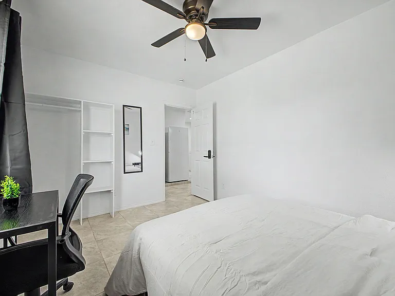 Private bedroom with ceiling fan, tile flooring, open closet shelving, and a compact desk area for work or study.