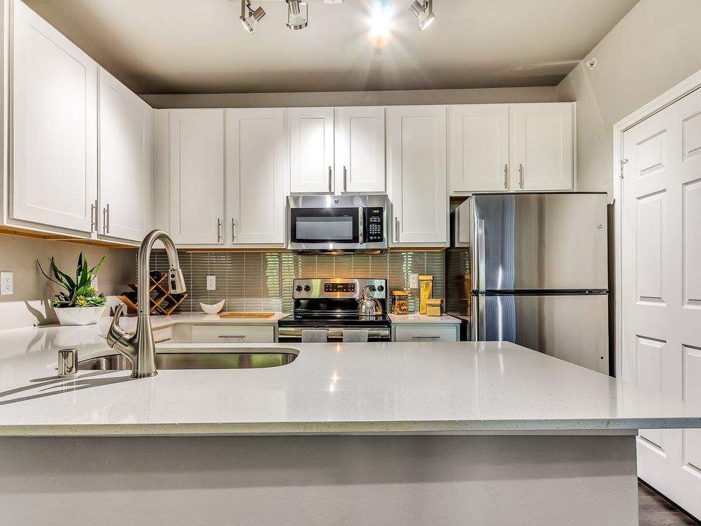Classic Package II kitchen with stainless steel appliances, white quartz countertop, tile backsplash, white cabinetry, and hard surface flooring