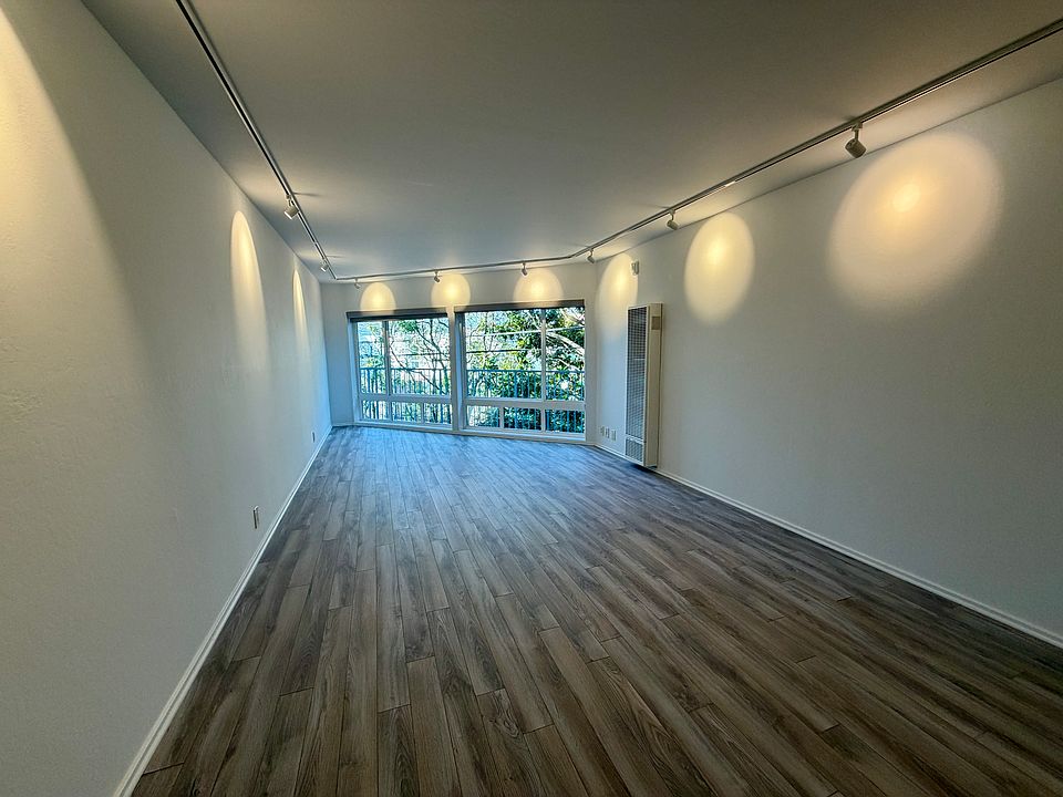 Open floor plan living space with a wall of windows framing leafy backyard views, creating a bright and tranquil setting.
