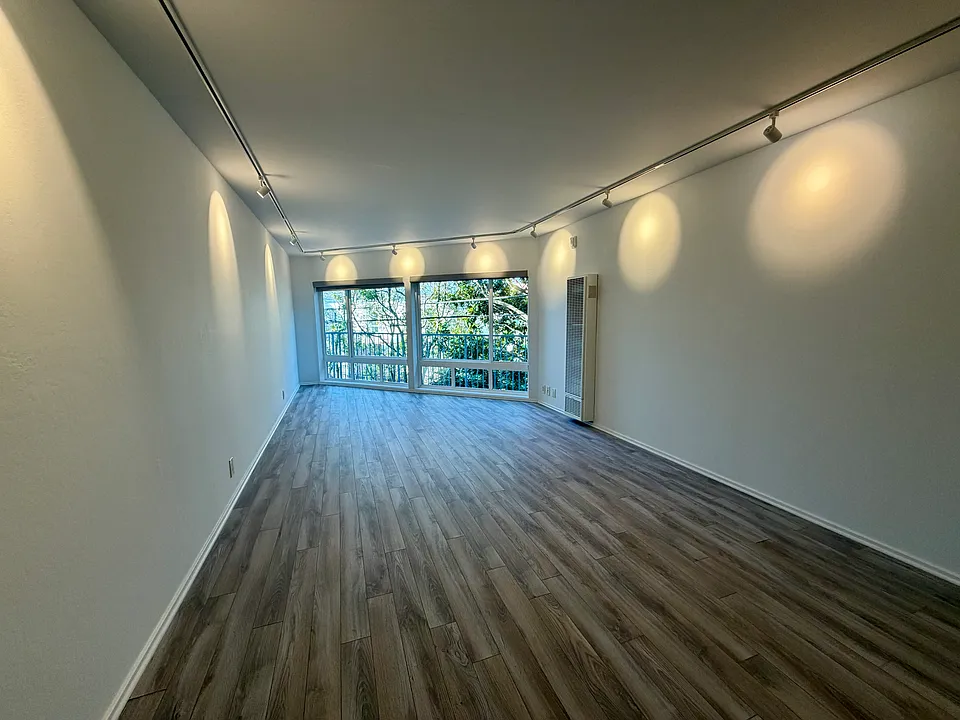 Open floor plan living space with a wall of windows framing leafy backyard views, creating a bright and tranquil setting.
