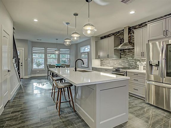 This beautiful kitchen has an oversized quartzite island, decorative back splash, sleek vent hood, undermount sink, and tons of storage.