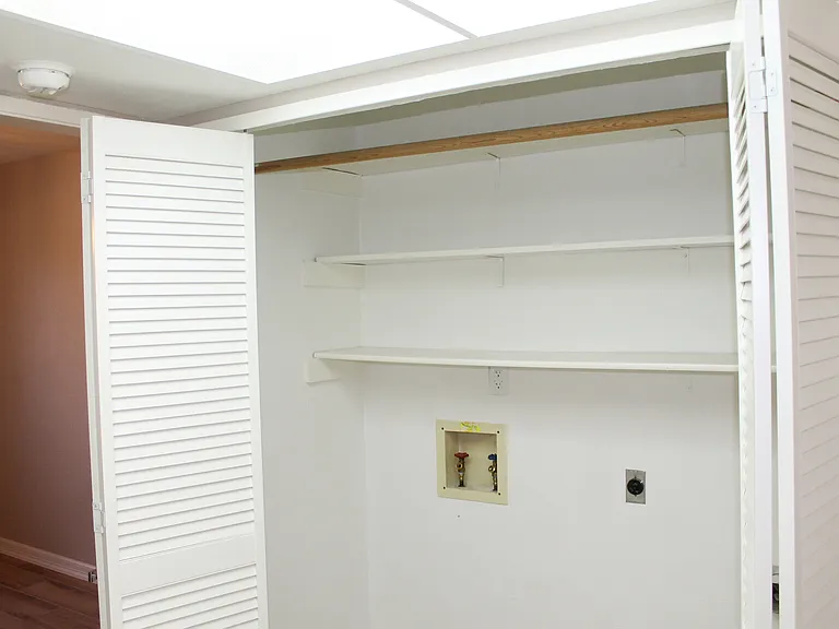 Dedicated laundry space tucked behind accordion doors, complete with washer and dryer hookups and plenty of shelving and a hanging rod.