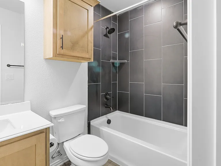 Bathroom featuring a white bathtub with dark gray subway tile surround, matte black shower fixtures, a light wood-finish vanity with an integrated sink, and a mirrored medicine cabinet