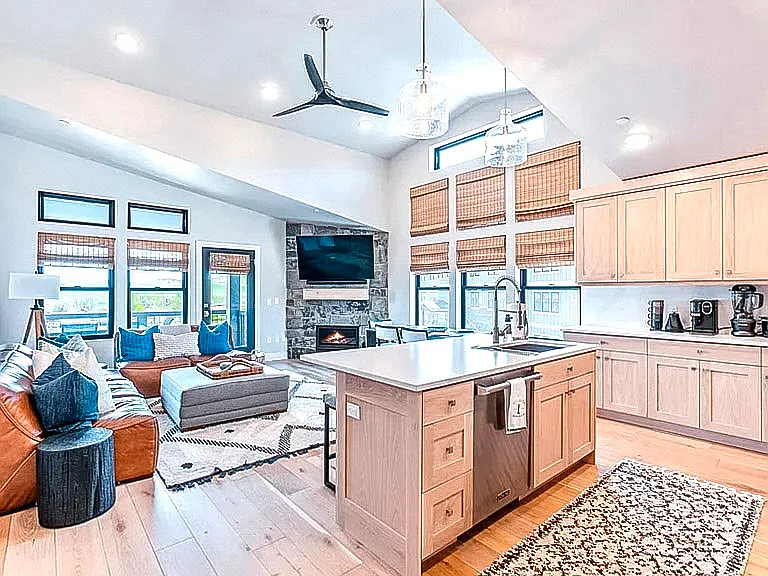 Expansive open-concept living and kitchen space with stone fireplace, large windows, and modern finishes throughout