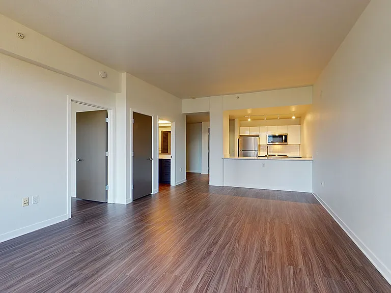 Apartment kitchen with stainless steel appliances, dining and living room with wood-style flooring.