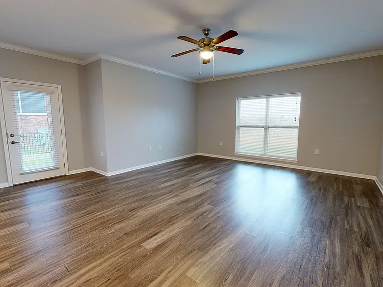 The Redbud layout includes a spacious living space with wood-style flooring, a large window, ceiling fan, and access to a private patio or balcony. The Redbud layout includes a spacious living space with wood-style flooring, a large window, ceiling fan, a