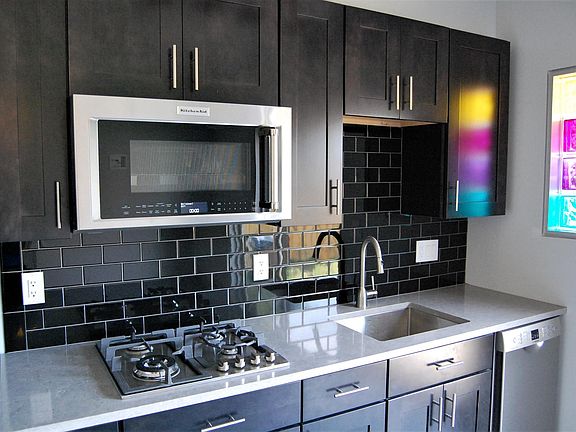 overview of kitchen area with stainless steel appliances, stone countertop and black subway tile backsplash